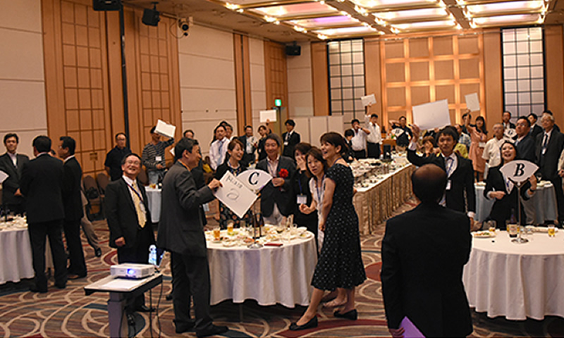 同じテーブルになった参加者で競い合った全員参加のクイズ　会場を盛り上げる伊藤・中部副支部長（左中央）