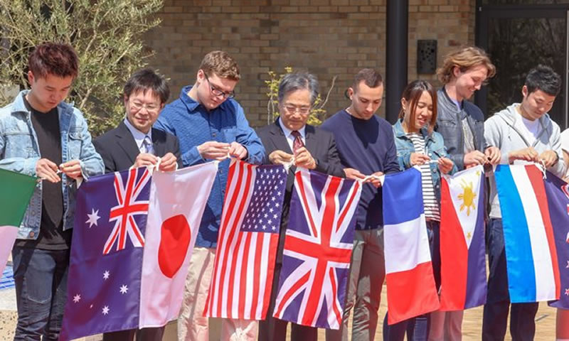 谷本学長や教授、留学生、本学学生で国旗を結びつけあう。左から３人目がケイレブ・マーサー君